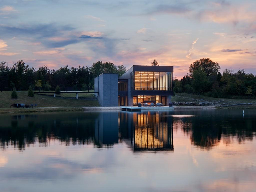 Across a lake, Treehuis is lit from within by interior lights at dusk